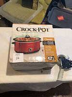 Box of Crock-Pot Classic slow cooker with red finish shown, a 6 quart capacity manual control slow cooker with removable stoneware and recipe book included.