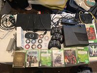 Full lot overview showing Xbox 360 console with controllers, PlayStation 3 console, various game discs and cases including Xbox 360 titles.