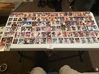 Wide shot of approximately 80 hockey trading cards spread out on a folding table, showing a large variety of players and teams in different poses and card styles.