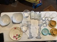 Table display of assorted houseware including bowls, decorative plates, glassware, candlesticks, and small decorative bowls.
