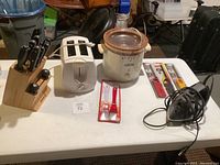 Wide shot of the lot showing knife block, toaster, crockpot, hand mixer and basting brushes on white table
