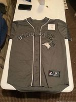 Grey MLB Toronto Blue Jays baseball jersey with button-up front, 'BLUE JAYS' text and logo patch on chest.