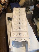 Tall white wooden jewelry cabinet with six drawers, each with floral carved design and crystal-like knob, shown lying flat.