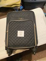 Front view of black Travelpro carry-on luggage on a white surface, showing quilted pattern and logo patch.