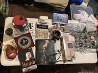 Overview of lot items showing clock, calculator, books, mask, jar, and other miscellaneous items on table.