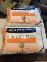 Two new Serta Ultimate Firm pillows sealed in plastic packaging showing brand, size, and specifications.