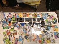 Top view of assorted Pokémon cards spread out on a table with some cards in sleeves and others loose, showing diverse types and colors.