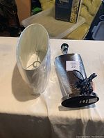 Table lamp parts, base separated from the shade, showing silver hammered metal finish and black base plate with power cord.