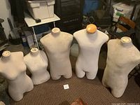 Five cloth-covered torso mannequins of varying sizes displayed on floor