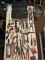 Full view of the lot showing socket set, wrenches, pliers, wire brushes, hammers, and other tools on a white surface.
