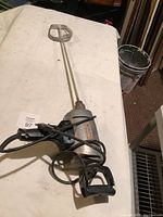 Full view of electric mixer with attached metal paddle on white surface.