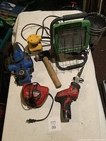 Lot of various tools on table including drill, sander, mallet, charger, planer, and light.