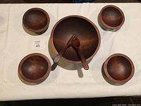 Top view of large wooden bowl with four smaller bowls surrounding it, with wooden salad fork and spoon inside large bowl.