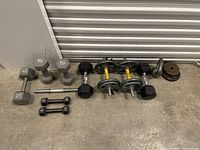 Overview of all dumbbells and weight plates laid out on floor showing variety and condition
