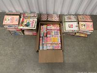 Top down view showing multiple stacks of manga books and a filled cardboard box with assorted manga volumes.