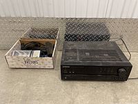 Pioneer VSX-305 audio/video stereo receiver and a box with assorted electronic components and cables on a grey floor.