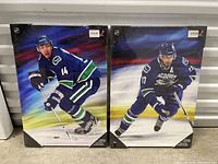 Two premium hockey prints side by side showing Vancouver Canucks players in action, shrink wrapped and ready for sale.