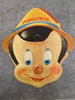 Front of Pinocchio mask showing painted face with hat labeled 'Pinocchio'.