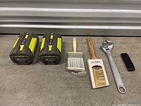 Two Ryobi 40V batteries, two paintbrushes, adjustable wrench, small black plastic hand tool on floor
