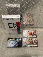 Photo showing sealed white Sony DX E-180 VHS tape box along with multiple sealed audio cassette tapes from TDK and Fuji.