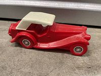 Front side view of red vintage Avon convertible car perfume bottle on concrete surface, showing right profile and white roof.