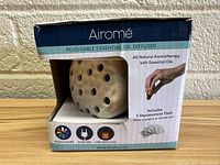 Front view of Airome diffuser in packaging showing product features and replacement pads included.