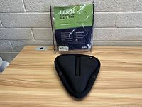 Photo showing the seat cover outside packaging on a tabletop with the original package in the background showing product details.