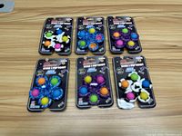 Six Bubble & Pop Stick & Pop Fidget toys on wooden table, assorted colors and shapes in original packaging.