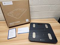 Etekcity smart fitness scale on a table next to its original box and user manuals.