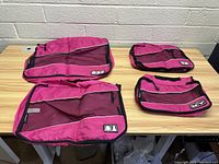 Four pink travel bags arranged on a wooden table, showing varying sizes and details of mesh and zipper