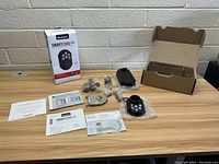 Photo showing Kwikset SmartCode 909 electronic deadbolt lock components including touchpad keypad, mounting hardware, lock mechanism, keys, manuals, and packaging box arranged on a wooden surface.
