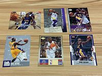 Overview of six Kobe Bryant Los Angeles Lakers basketball cards laid out on wood table.