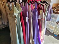 Photo of dresses on hangers showing variety of colors including pastel greens, reds, purples, and creams.