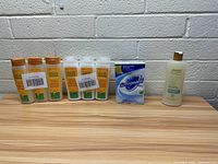 Seven bottles of shampoo, conditioner and soaps and one body lotion bottle on wooden surface in front of white brick wall.