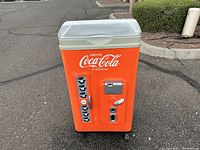 Front view of orange Coca-Cola rolling ice chest cooler with coin slot and 'Drink Coca-Cola in Bottles' text.