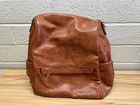 Front view of the brown faux leather women's backpack purse showing the smooth texture and front pocket flap.