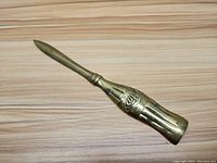 Top down photo of the vintage brass Coca Cola bottle shaped letter opener on wooden surface showing embossed details.