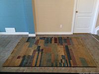 Full view showing the entire rectangular area rug with geometric block pattern in various muted earth-tone and blue colors.