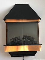 Front view of the Dimplex electric fireplace showing the black top, copper-tone trim, glass front, and logs inside.