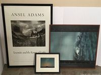 Three framed photographs displayed against white background: large Ansel Adams landscape, medium gray wolf photo by Branden Burg, and small comet photo.