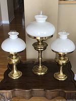 Three hurricane table lamps displayed on a wooden surface, showing the full set including one large lamp and two smaller matching lamps.