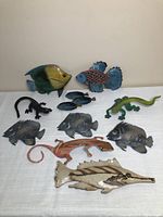 Photo of various metal wall decor items arranged on a white surface including colorful fish and lizards for size and detail.