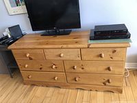 Front view of pine dresser showing seven drawers, wooden knobs, and scalloped base with electronics on top not included.
