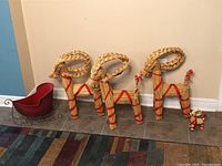 Set of three large straw reindeer with braided antlers, red ribbon detailing, one small reindeer, and a red decorative metal sleigh on tile floor near wall