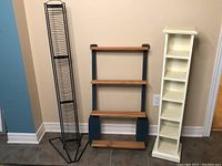 Photo showing three shelving units side by side: black metal CD rack, decorative paddle shelf, and white wooden CD rack.