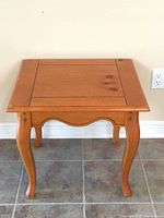 Palliser pine side table viewed frontally showing curved legs and paneled top with wood knots.