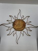 Front view of large metal sun wall hanging showing sun face and flame-like rays in golden bronze tone.