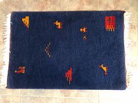 Top down view of dark blue wool rug with colorful geometric animal patterns and fringes on short sides.