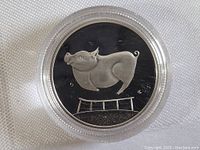 Reverse of the coin with pig motif leaping over a fence, shown on black background.