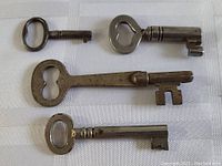 Four antique metal skeleton keys of various sizes and shapes placed on a white cloth background, showing different bow designs and key shafts.